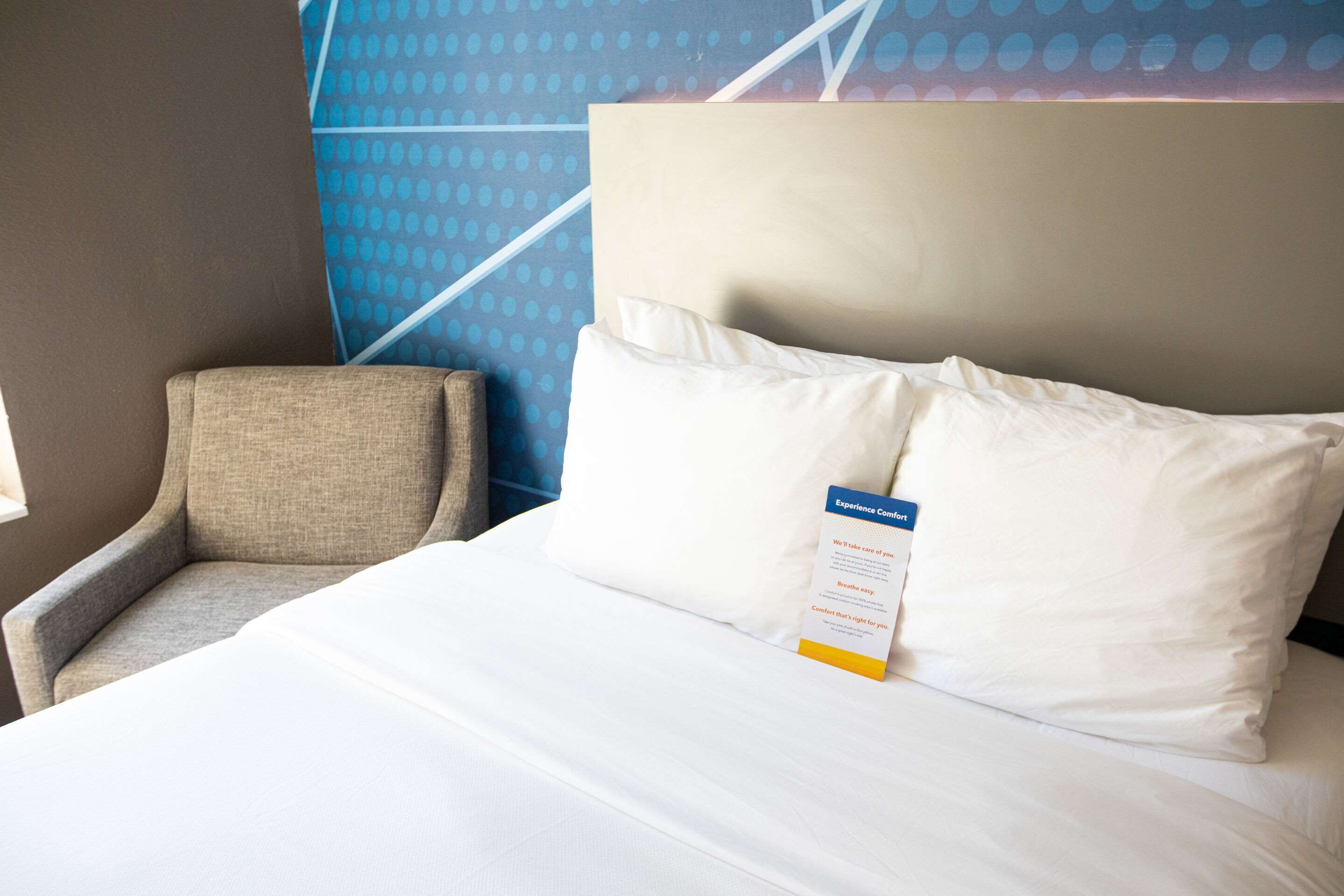 A hotel room with a bed, a pillow, a chair, and a wall with a blue polka dot pattern.