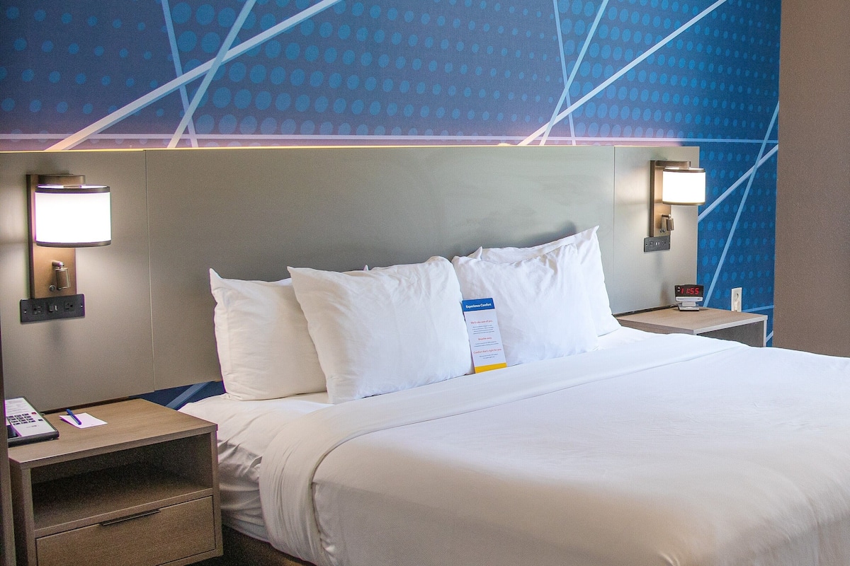 A hotel room with a large bed, two bedside tables, a nightstand, and a wall with a geometric pattern.