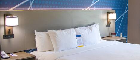 A hotel room with a large bed, two bedside tables, a nightstand, and a wall with a geometric pattern.