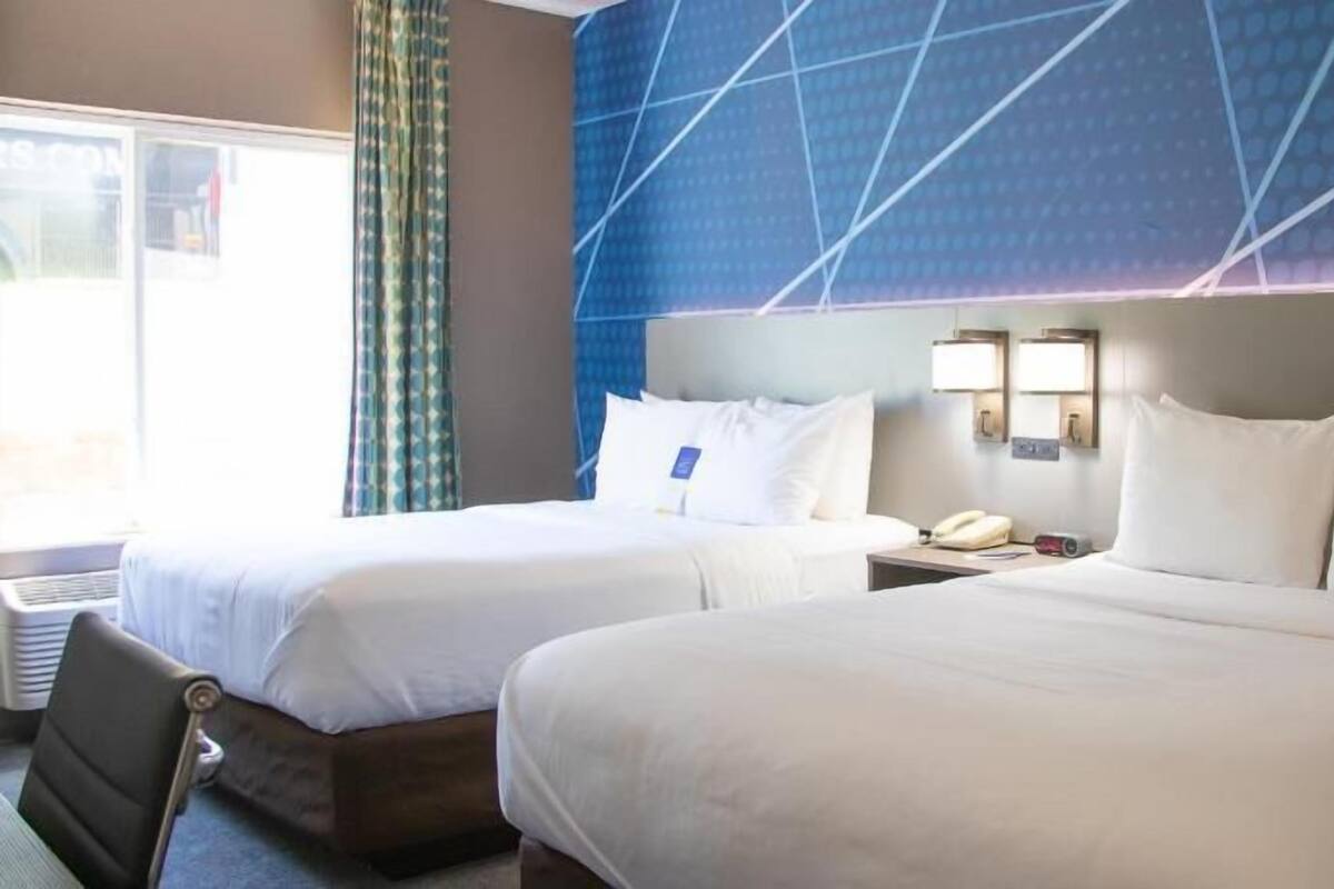 A hotel room with two beds, a window, a wall-mounted phone, and a wall-mounted light fixture.