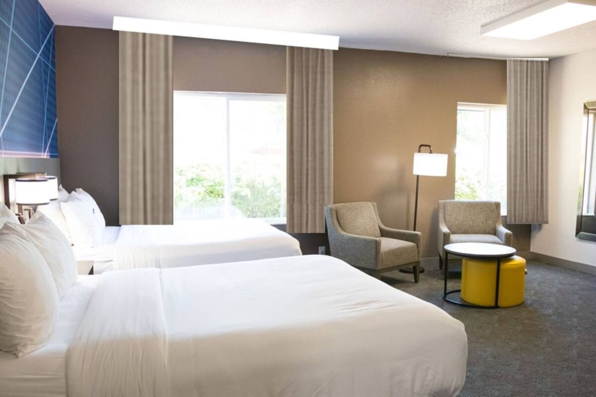A hotel room with two beds, a chair, a small round table, and a lamp.