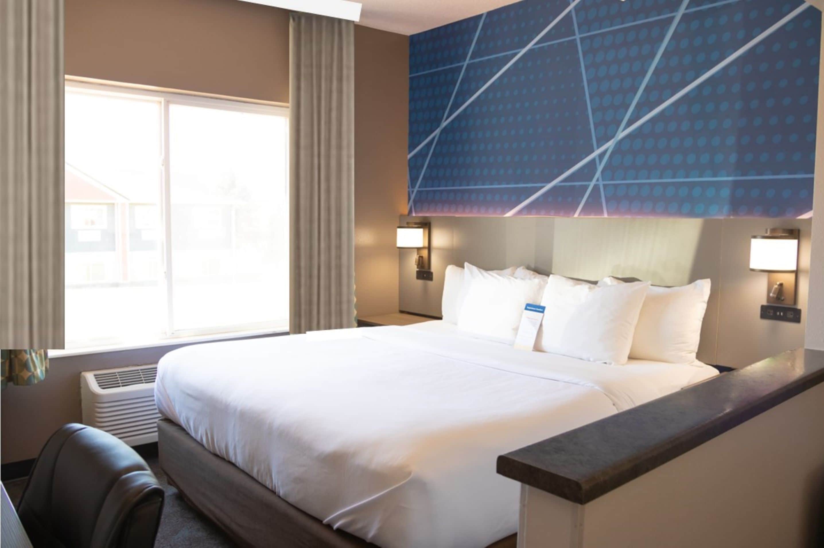A hotel room with a large bed, a desk, a chair, and a window with curtains.