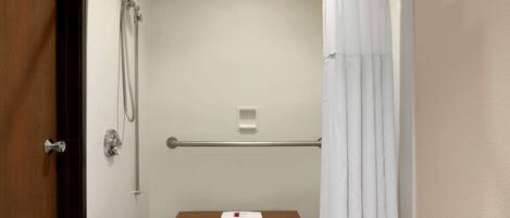 A bathroom with a shower, a toilet, and a bench with a towel.