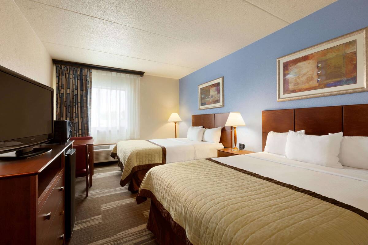 Une chambre d’hôtel avec deux lits, une télévision, un bureau et une fenêtre avec des rideaux.