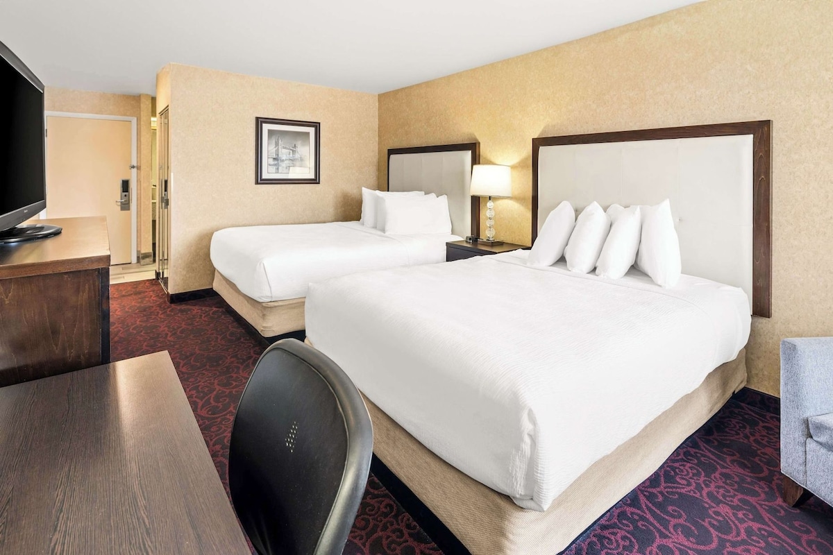 A hotel room with two beds, a desk, a chair, and a television.