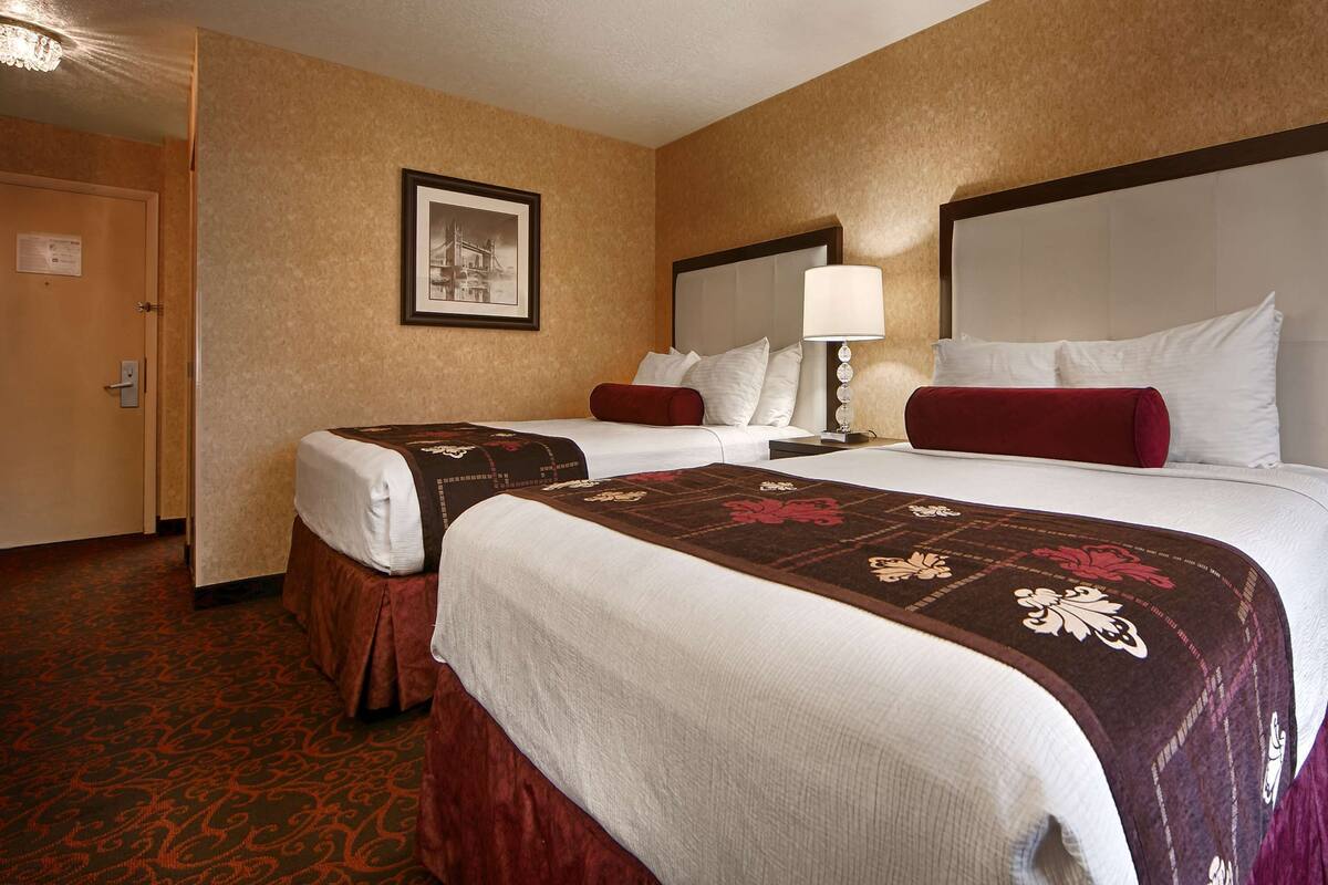 A hotel room with two beds, a large mirror, a framed picture on the wall, and a carpeted floor.