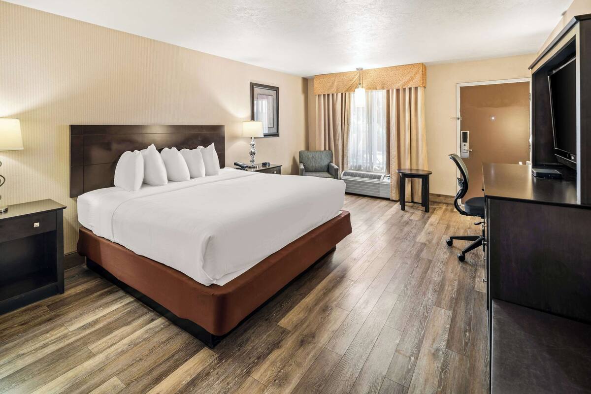 A hotel room with a large bed, a desk with a chair, a television, and an air conditioning unit.