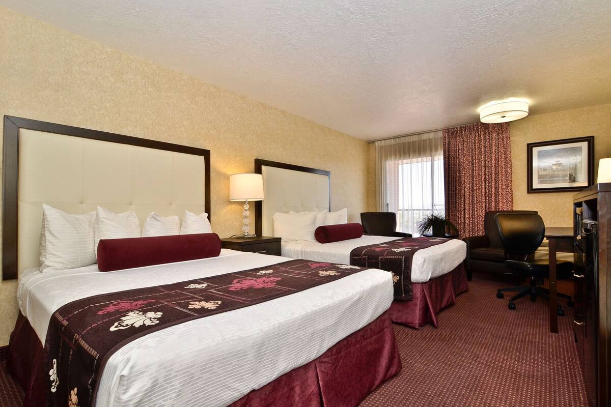 A hotel room with two beds, a desk, and a chair.