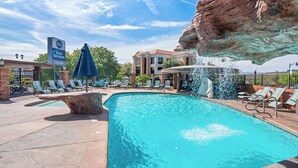 A pool area with lounge chairs, a sign for Best Western Coral Hills, and a rock formation above the pool. - Best Western Coral Hills (St. George)