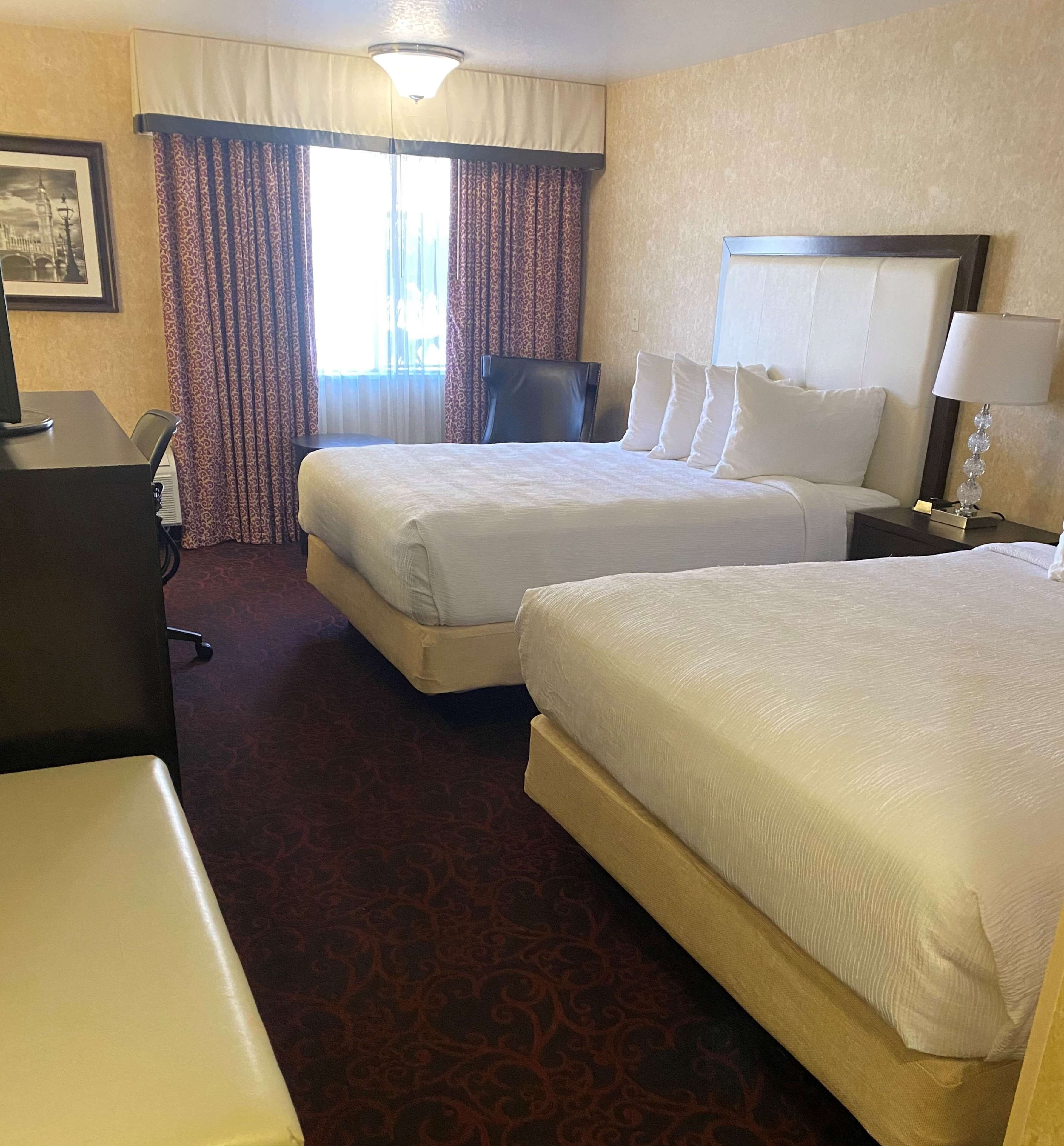 A hotel room with two beds, a desk, a chair, and a lamp.