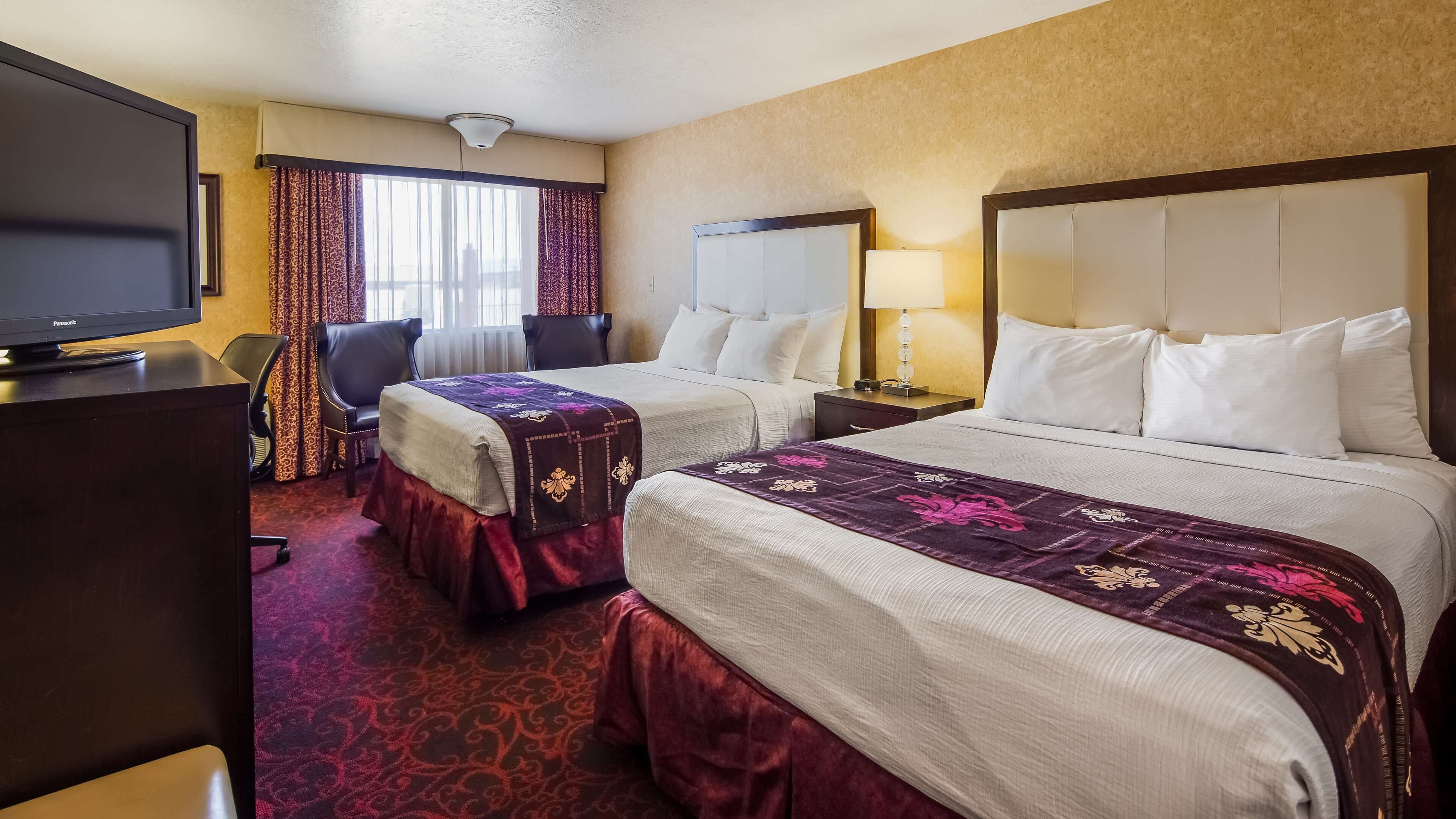 A hotel room with two beds, a desk with a television, a chair, and a window with curtains.