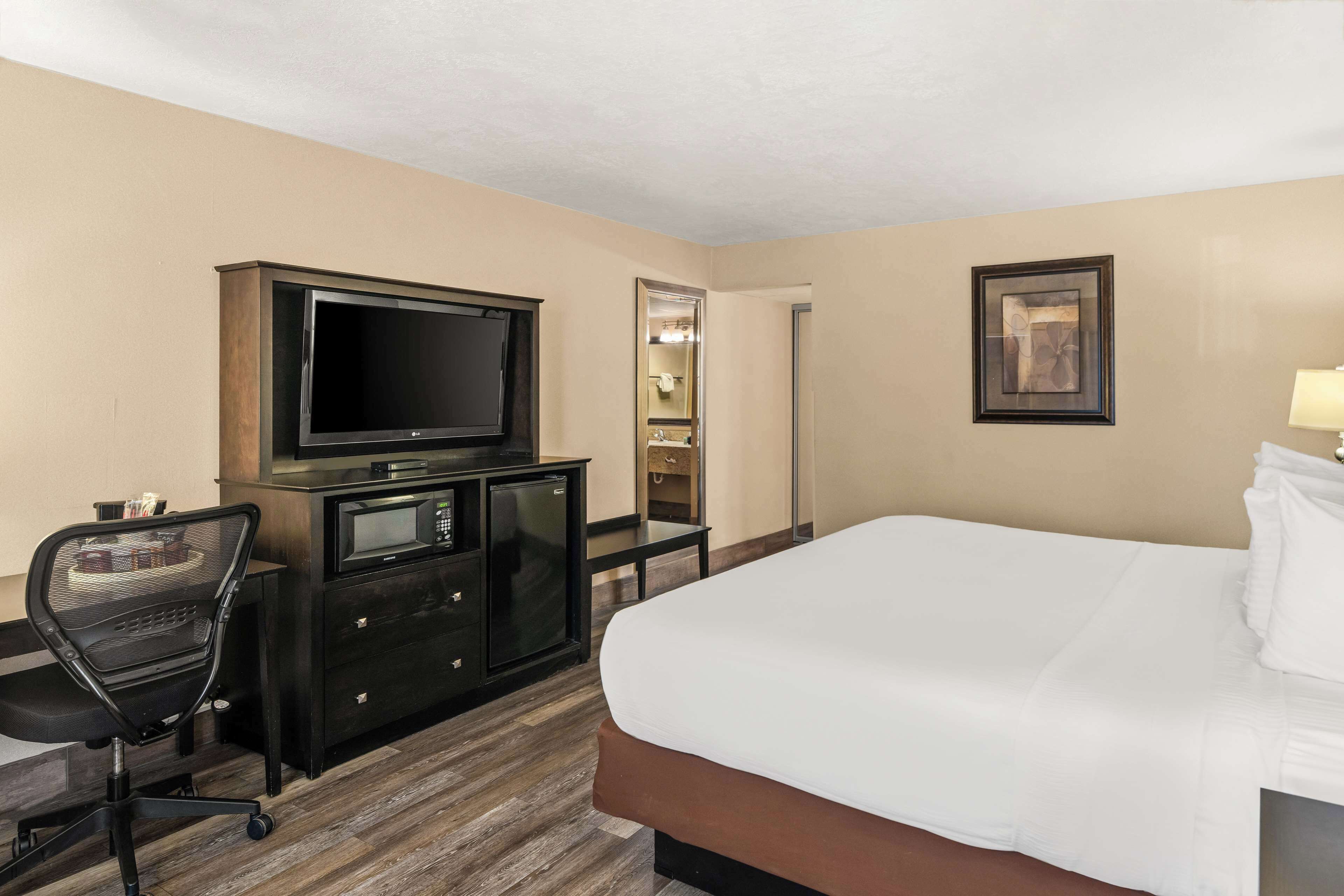 A hotel room with a bed, a desk with a television, a chair, a wardrobe, and a mirror.