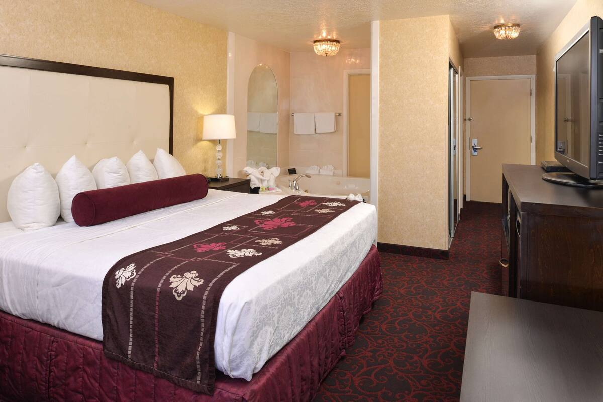 A hotel room with a large bed, a television, and a bathroom with a bathtub and a mirror.