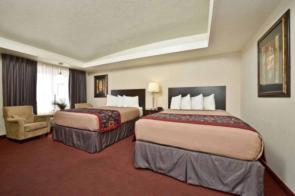 A hotel room with two beds, a chair, a lamp, and a framed picture on the wall.