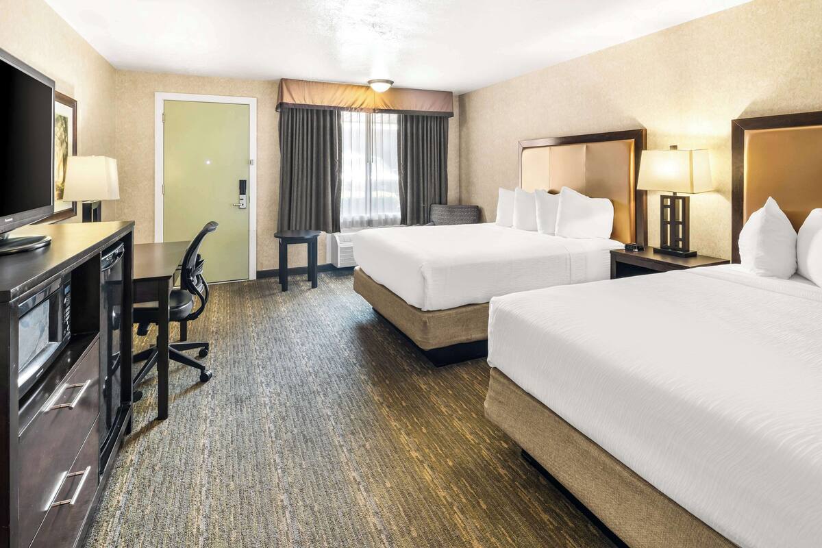 A hotel room with two beds, a desk with a chair, a television, and a lamp.