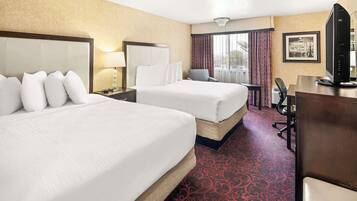 Quarto de hotel com duas camas, uma escrivaninha, uma cadeira, televisão e janela com cortinas.