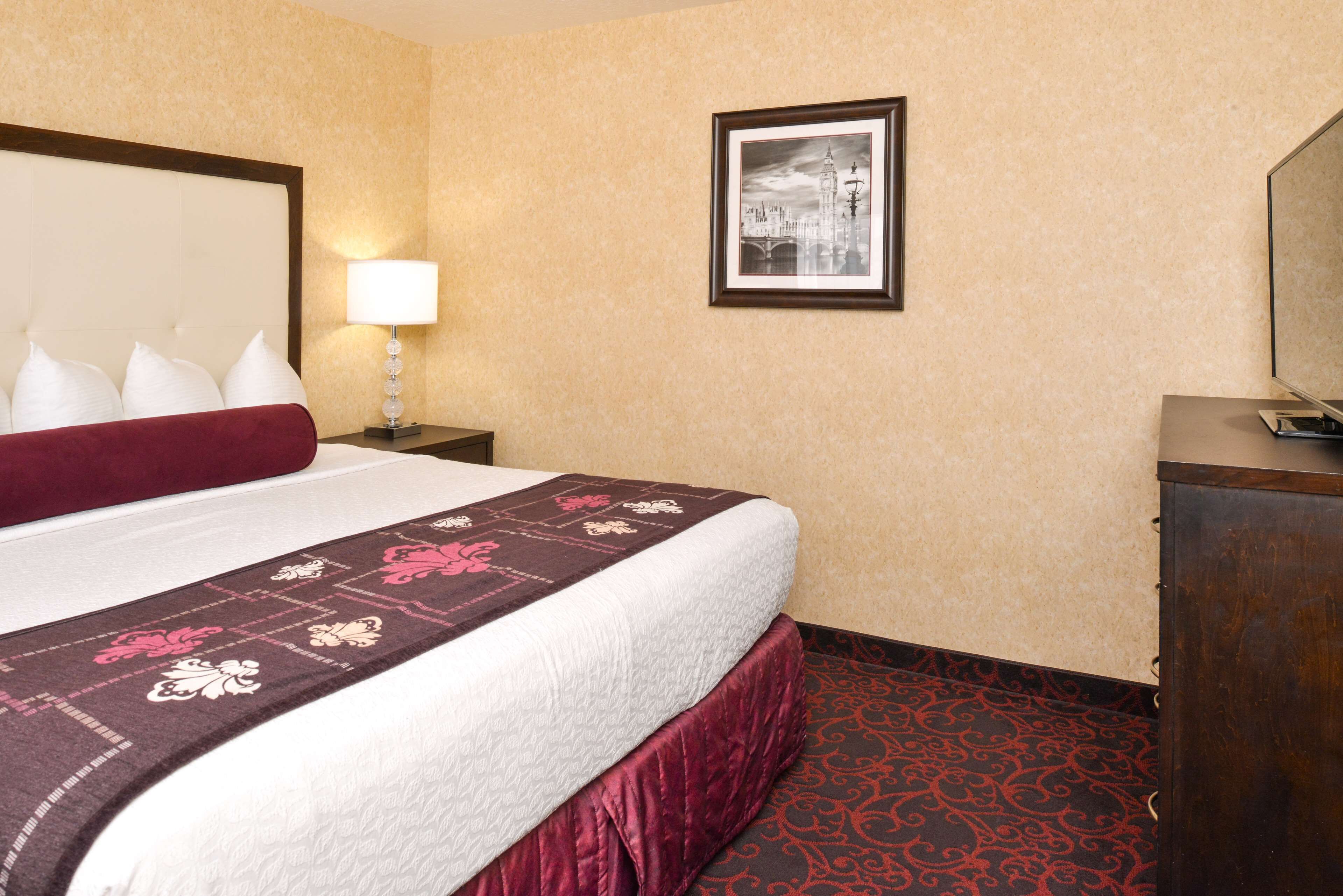 A hotel room with a large bed, a nightstand with a lamp, a framed picture on the wall, and a wooden dresser.