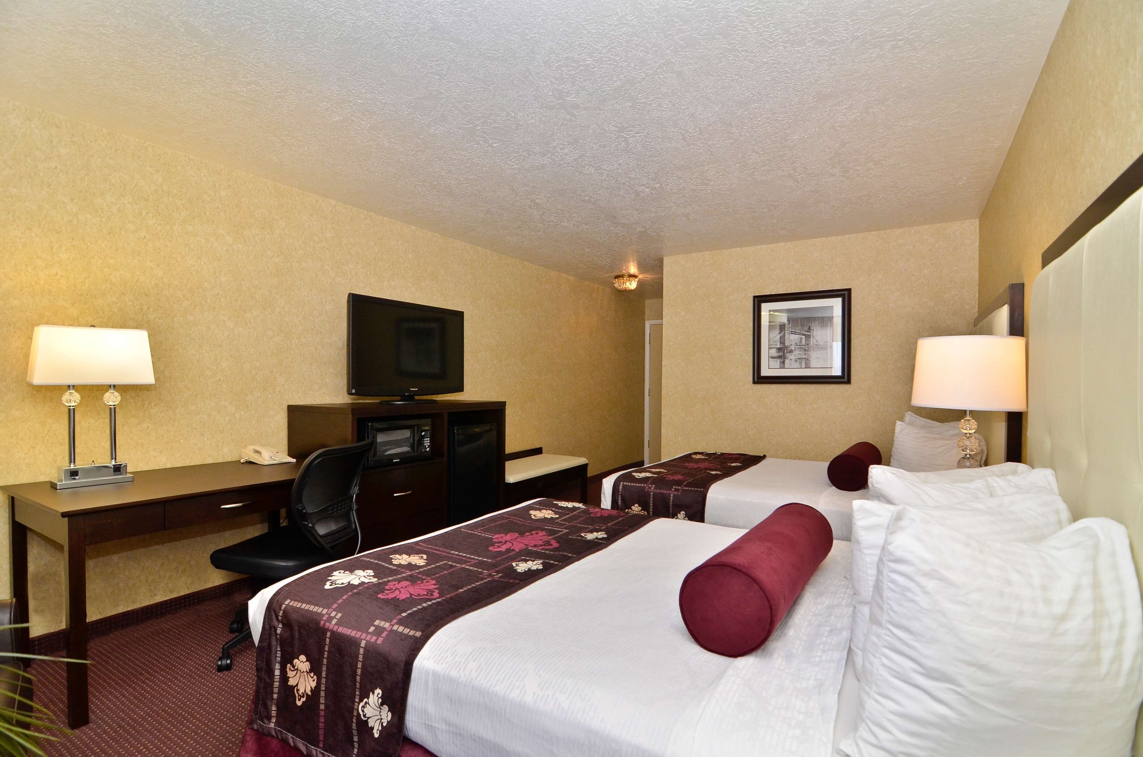 A hotel room with two beds, a desk, a television, and a framed picture on the wall.