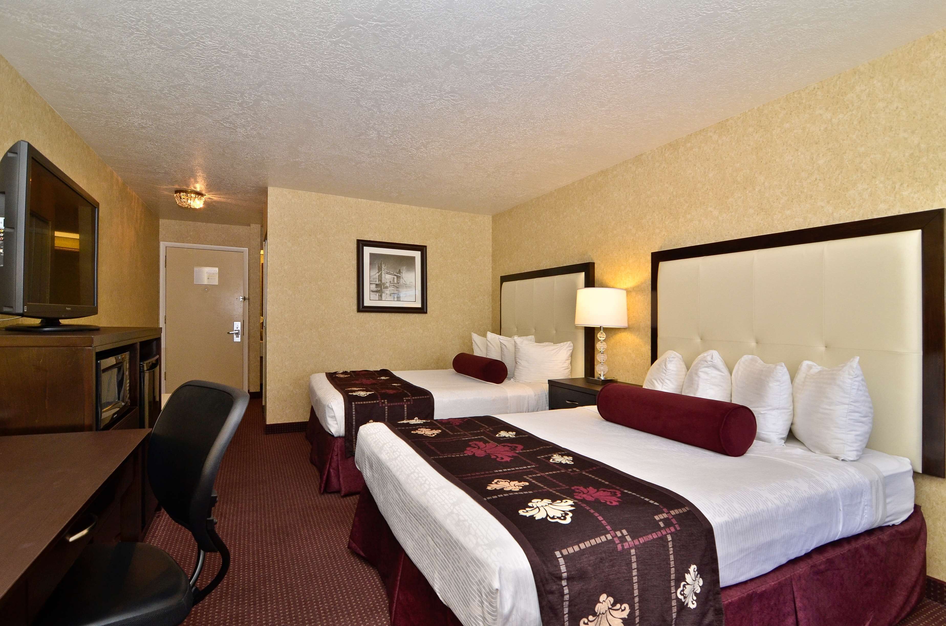 A hotel room with two beds, a desk with a chair, a television, and a framed picture on the wall.