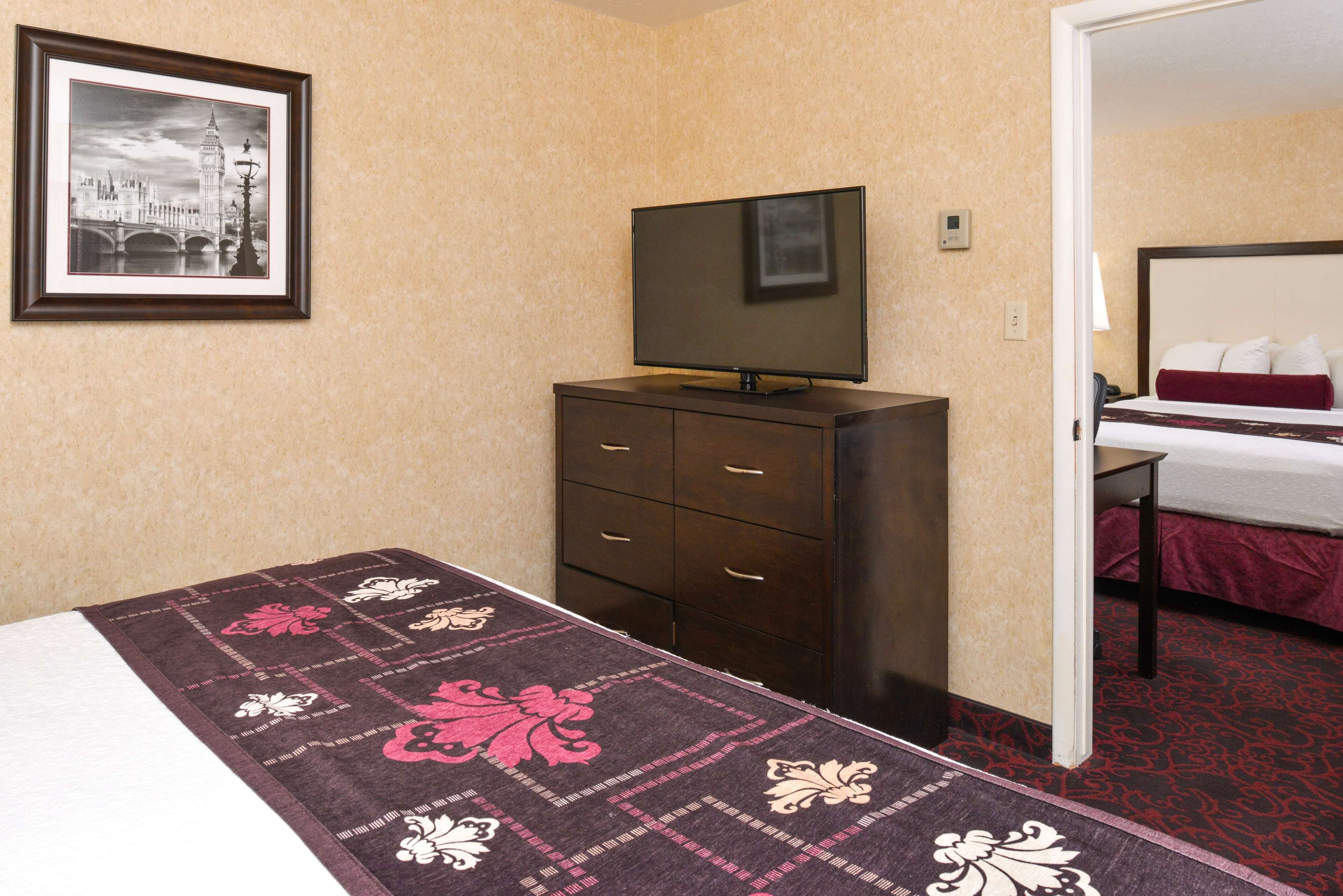 Habitación de hotel con cama, cómoda, televisor y un cuadro enmarcado de un paisaje urbano.