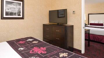 Habitación de hotel con cama, cómoda, televisor y un cuadro enmarcado de un paisaje urbano.