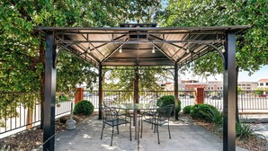 A covered outdoor seating area with a table and chairs, surrounded by a metal fence and greenery. - Best Western Coral Hills (St. George)