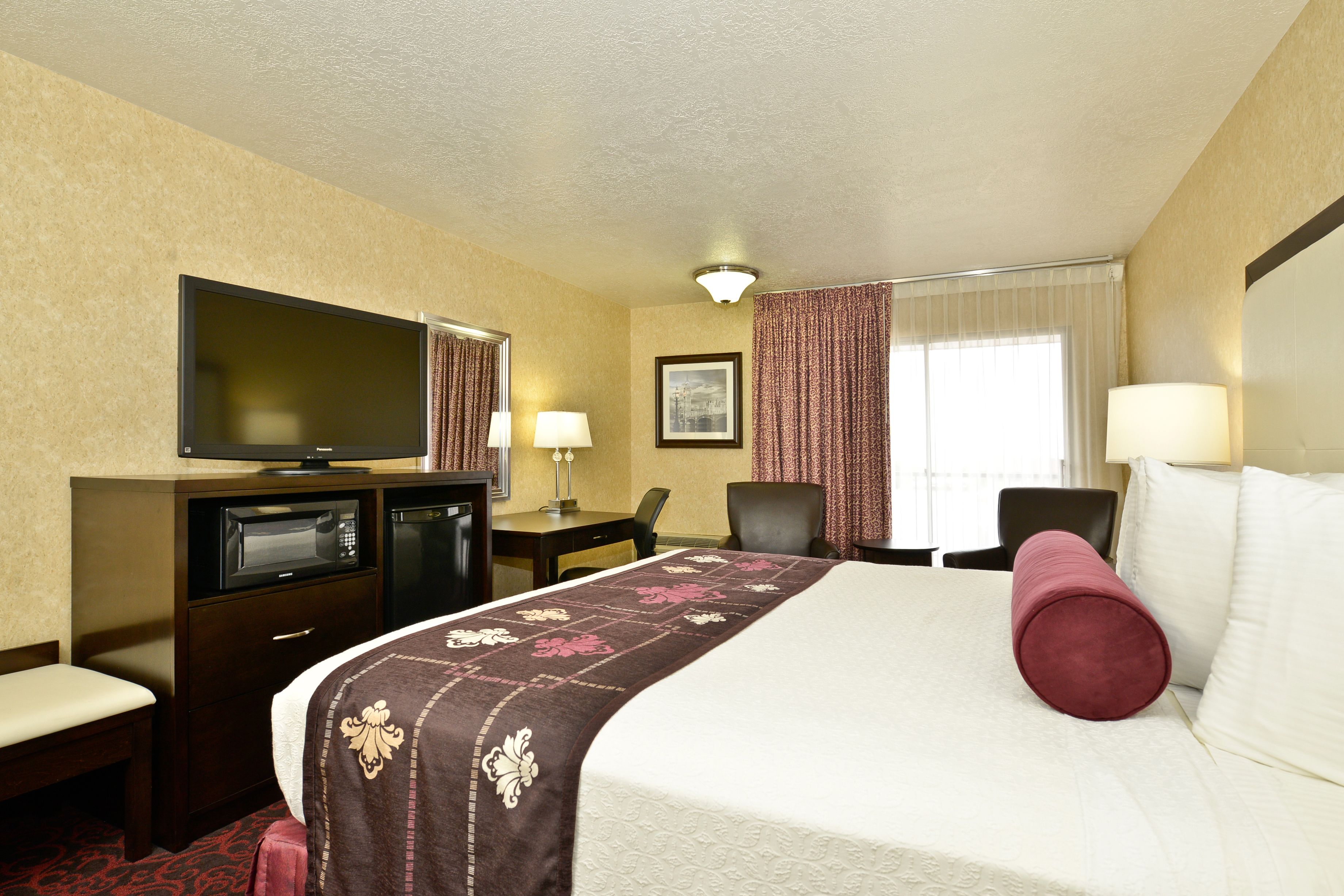 Ein Hotelzimmer mit einem Bett, einem Fernseher, einem Schreibtisch mit Stuhl und einem Vorhangfenster.