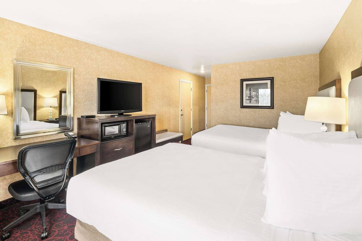 A hotel room with two beds, a desk with a TV, a chair, and a mirror.