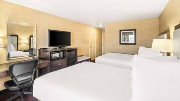 Ein Hotelzimmer mit zwei Betten, einem Schreibtisch mit Fernseher, einem Sessel und einem Spiegel.