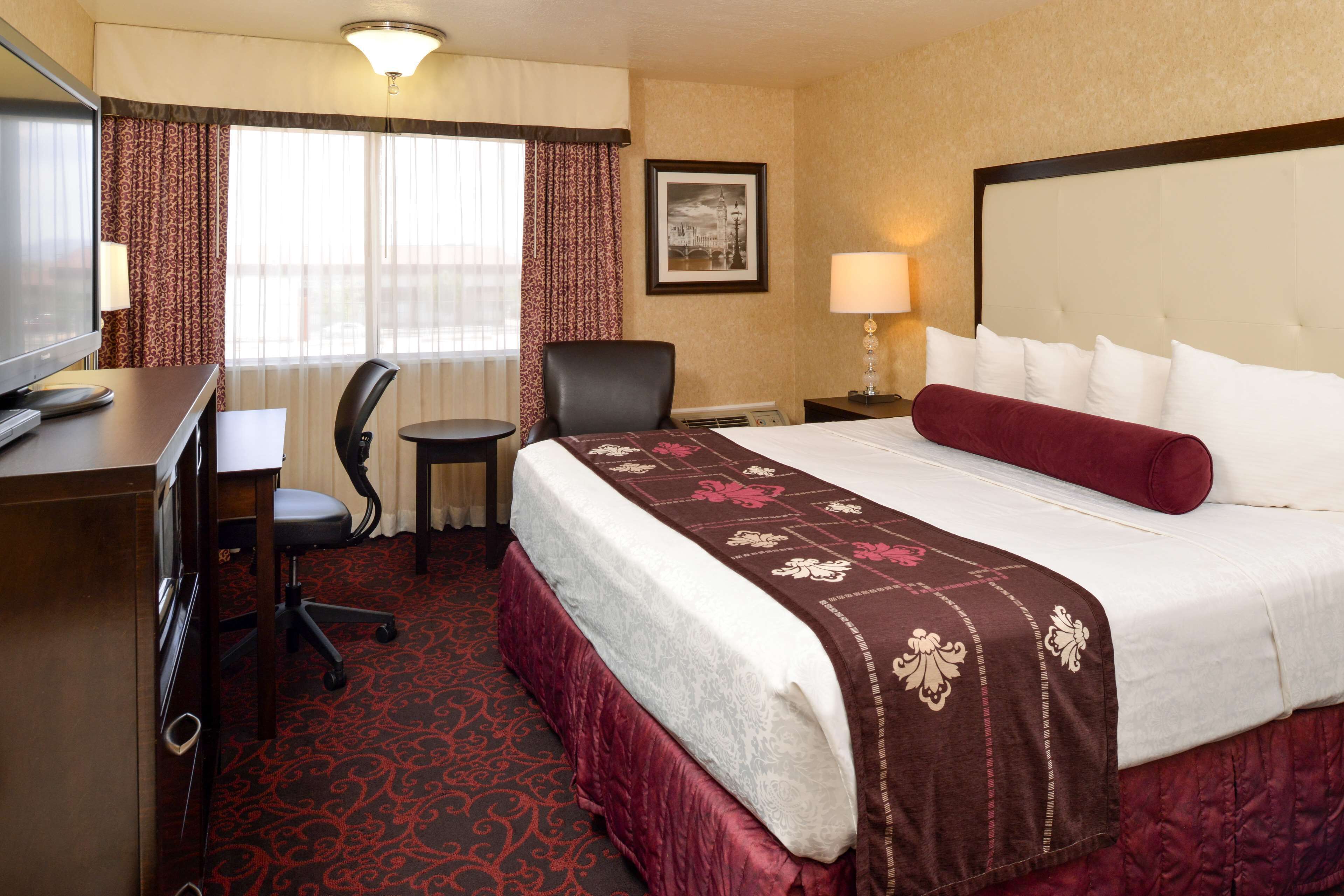 A hotel room with a bed, a desk, a chair, a TV, and a window with curtains.