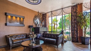A modern living room with leather sofas, a coffee table, and a large window with patterned curtains. - Best Western Coral Hills (St. George)