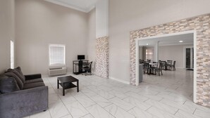 A spacious living area with a grey sofa, a coffee table, and a TV. There is a dining area with a table and chairs visible through an open doorway. - Super 8 by Wyndham Covington (Covington)