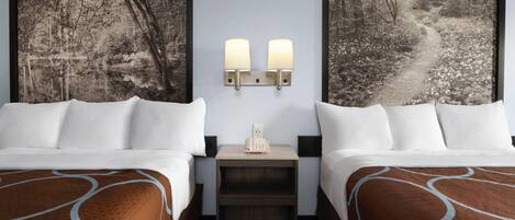 Ein Hotelzimmer mit zwei Betten, einem Nachttisch mit Lampe und zwei gerahmten Bildern an der Wand.