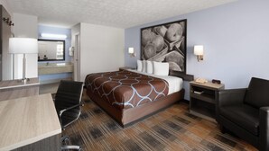 A hotel room with a large bed, a desk, a chair, a nightstand, and a wall-mounted lamp. - Super 8 by Wyndham Covington (Covington)