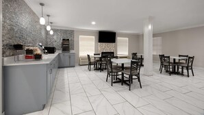 A modern kitchen with a marble countertop, a dining area with a white table and dark chairs, and a stone backsplash. - Super 8 by Wyndham Covington (Covington)