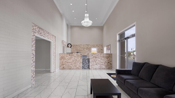 A spacious living area with a dark sofa, a black coffee table, and a tiled floor. There is a brick accent wall and a large window providing natural light. - Super 8 by Wyndham Covington (Covington)