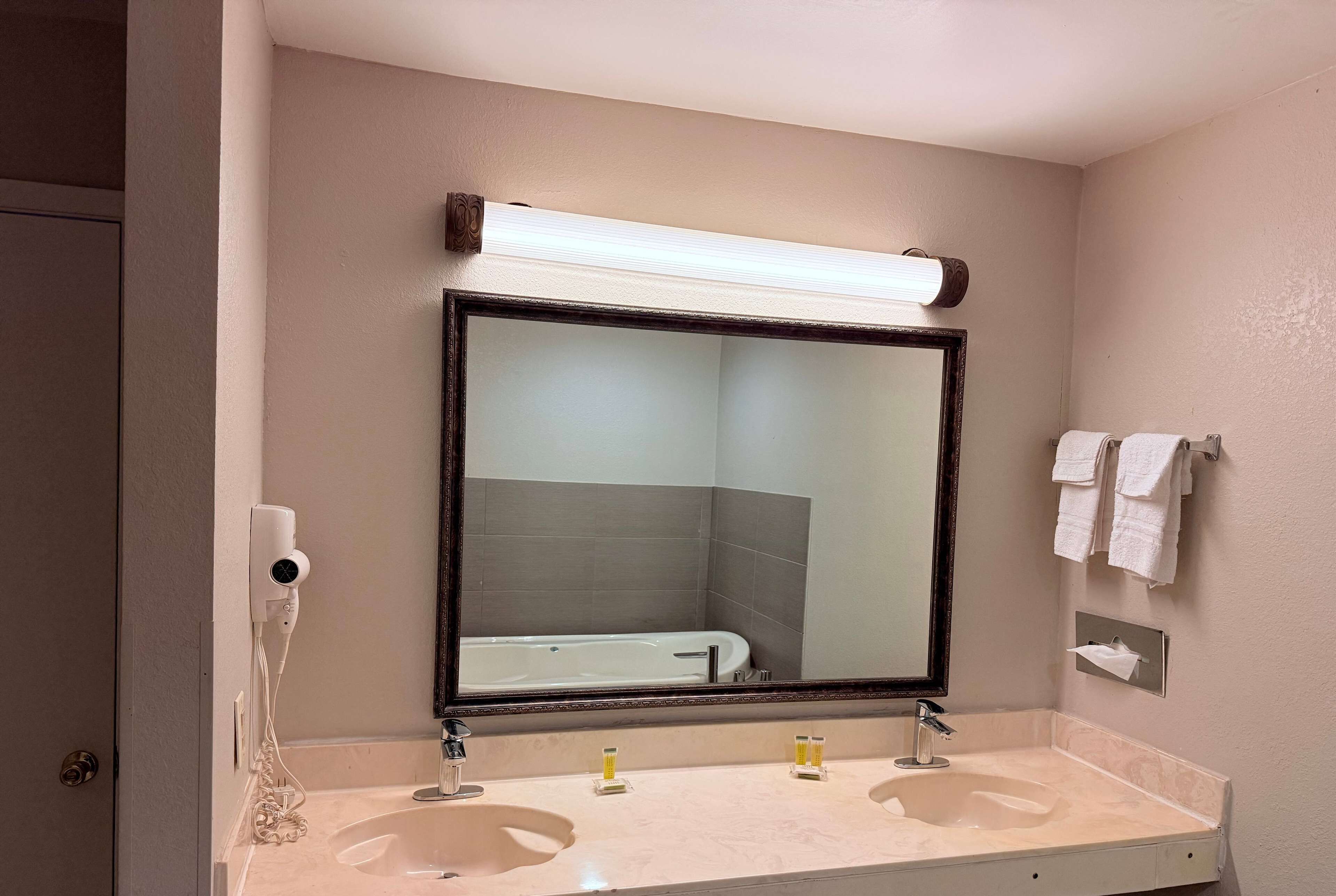 A bathroom with a large mirror, two sinks, a hairdryer, and towels on the wall.