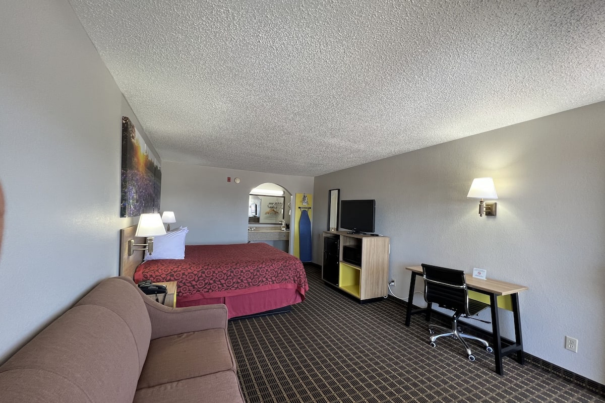 Quarto de hotel com cama, escrivaninha, cadeira, televisão e abajur.
