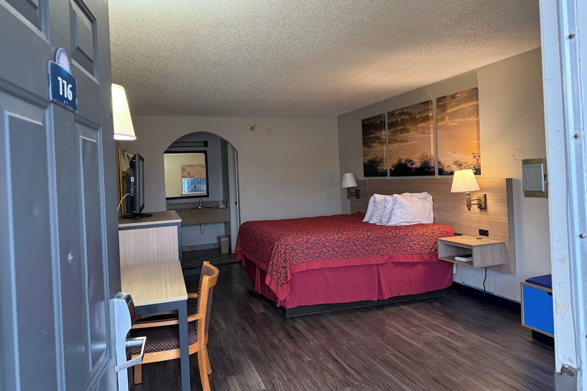 Quarto de hotel com cama, escrivaninha, cadeira e um quadro na parede.