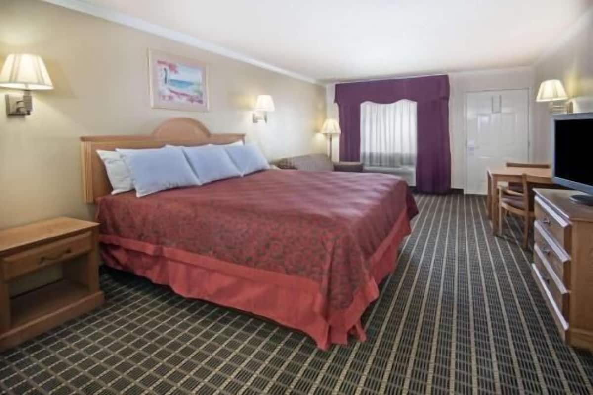 Quarto de hotel com cama, mesas de cabeceira, televisão, escrivaninha e janela com cortinas.