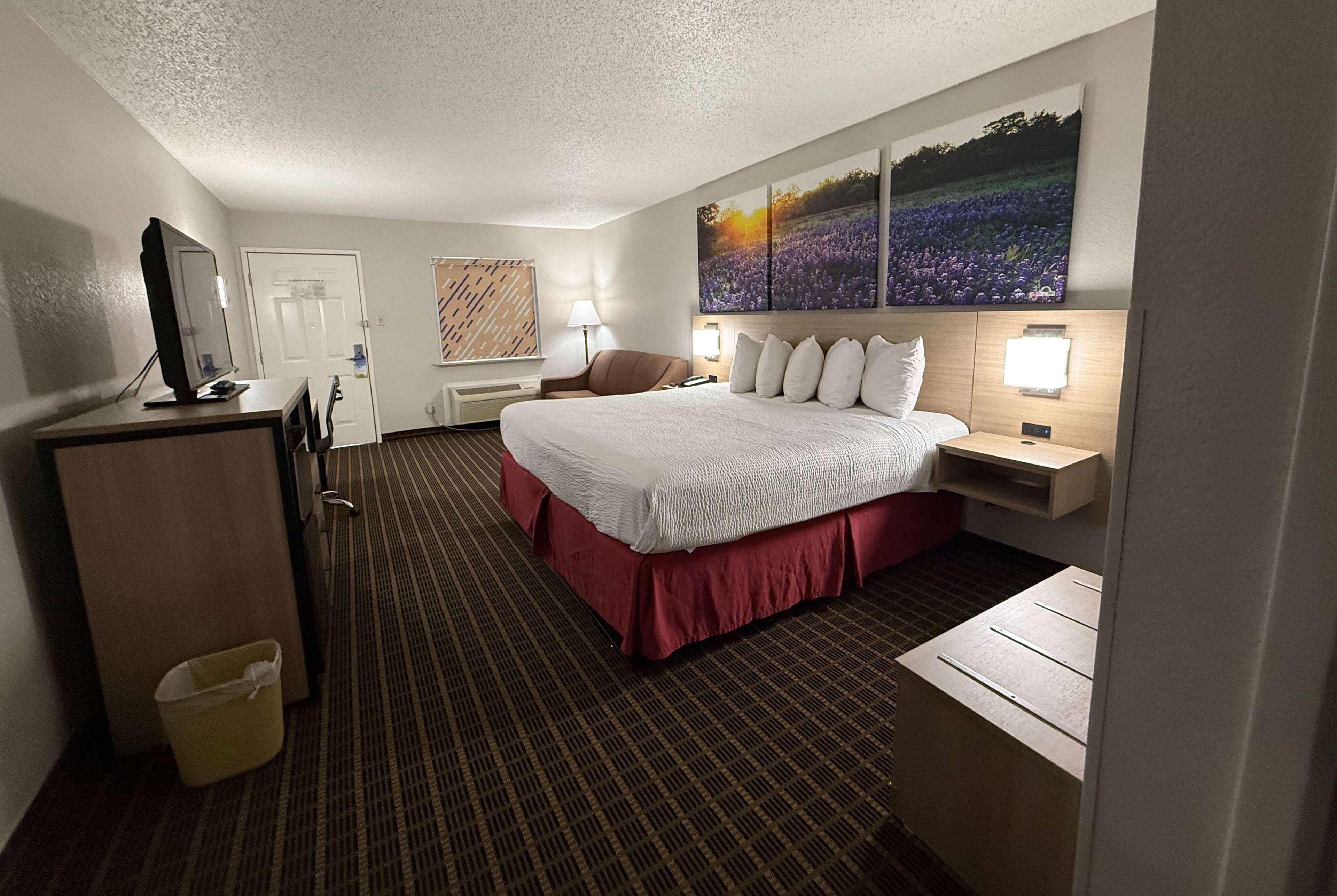 A hotel room with a large bed, a desk, a chair, a TV, and a painting on the wall.