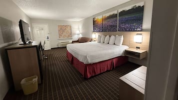 Una habitación de hotel con una cama grande, un escritorio, una silla, un televisor y un cuadro en la pared.