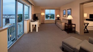 A hotel room with a large window, a sofa, a table, and a TV.