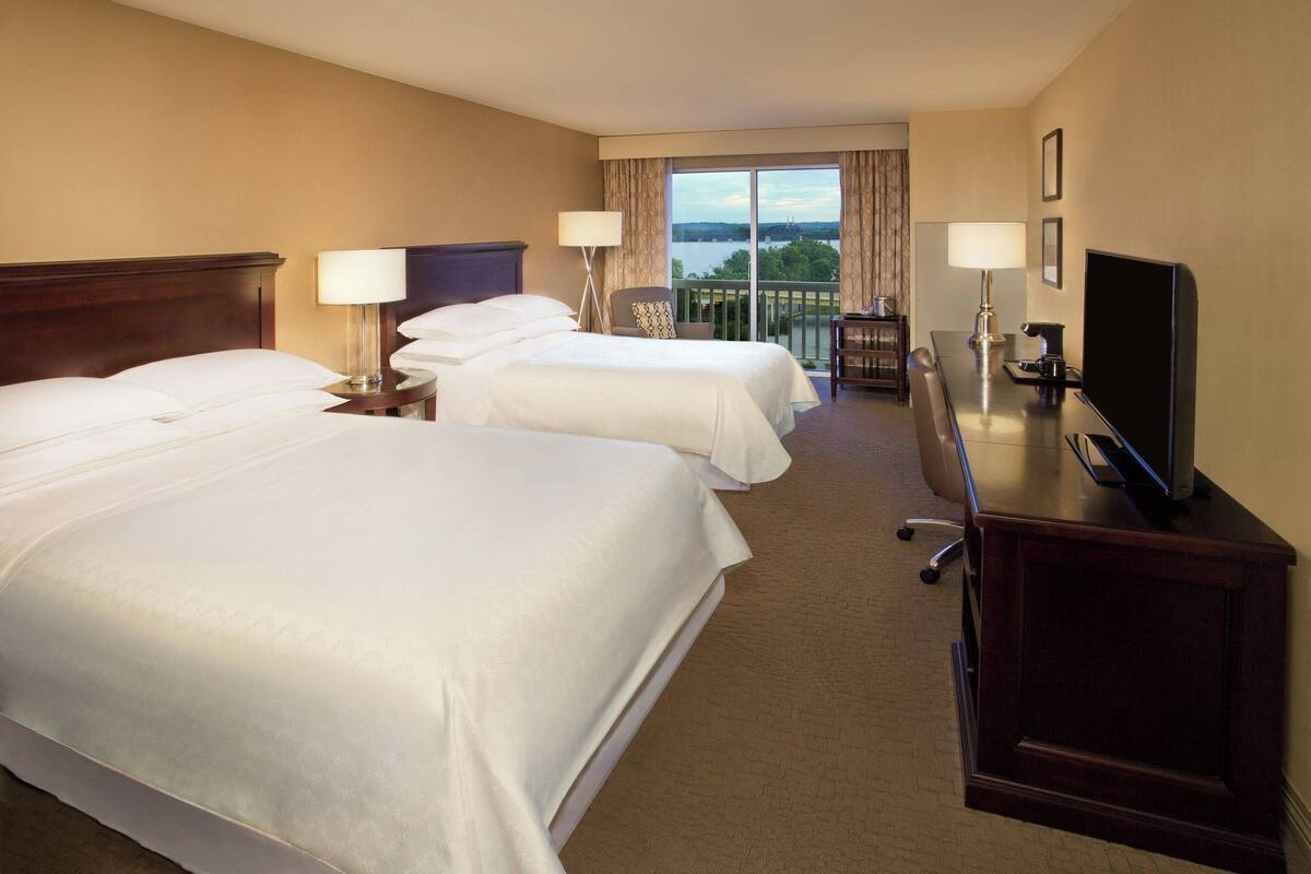 A hotel room with two beds, a desk with a television, and a view of the outdoors.