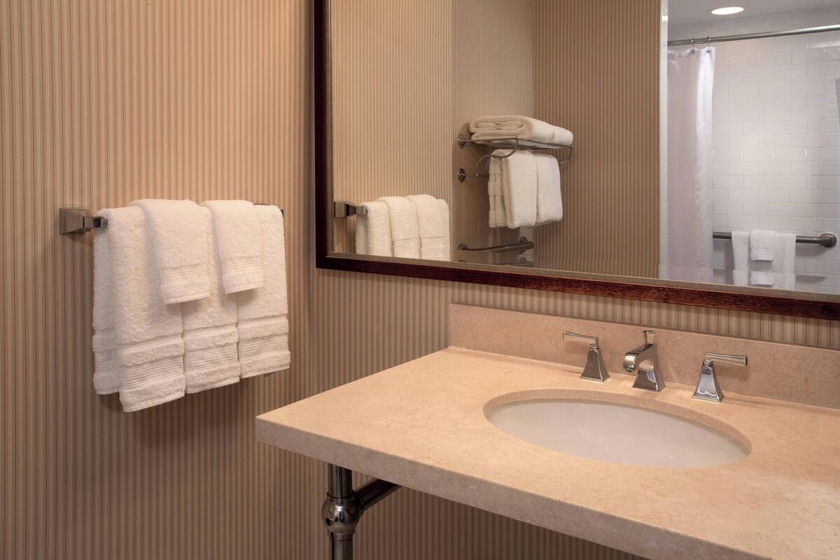 A bathroom with a beige sink, two faucets, and a mirror.