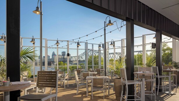 An outdoor seating area with tables and chairs, large windows, and string lights.