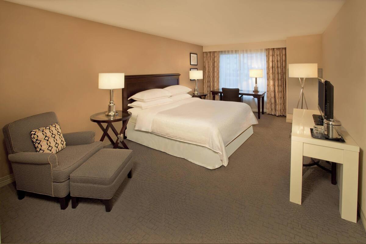 A hotel room with a bed, a sofa, a chair, a desk, and a television.