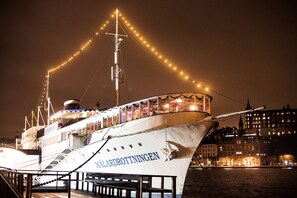 Un barco grande iluminado amarrado en un muelle, con un paisaje urbano de fondo.