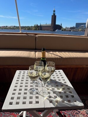 Una mesa con una botella de champán y copas en la cubierta de un barco, con vistas a un paisaje urbano y una torre destacada.