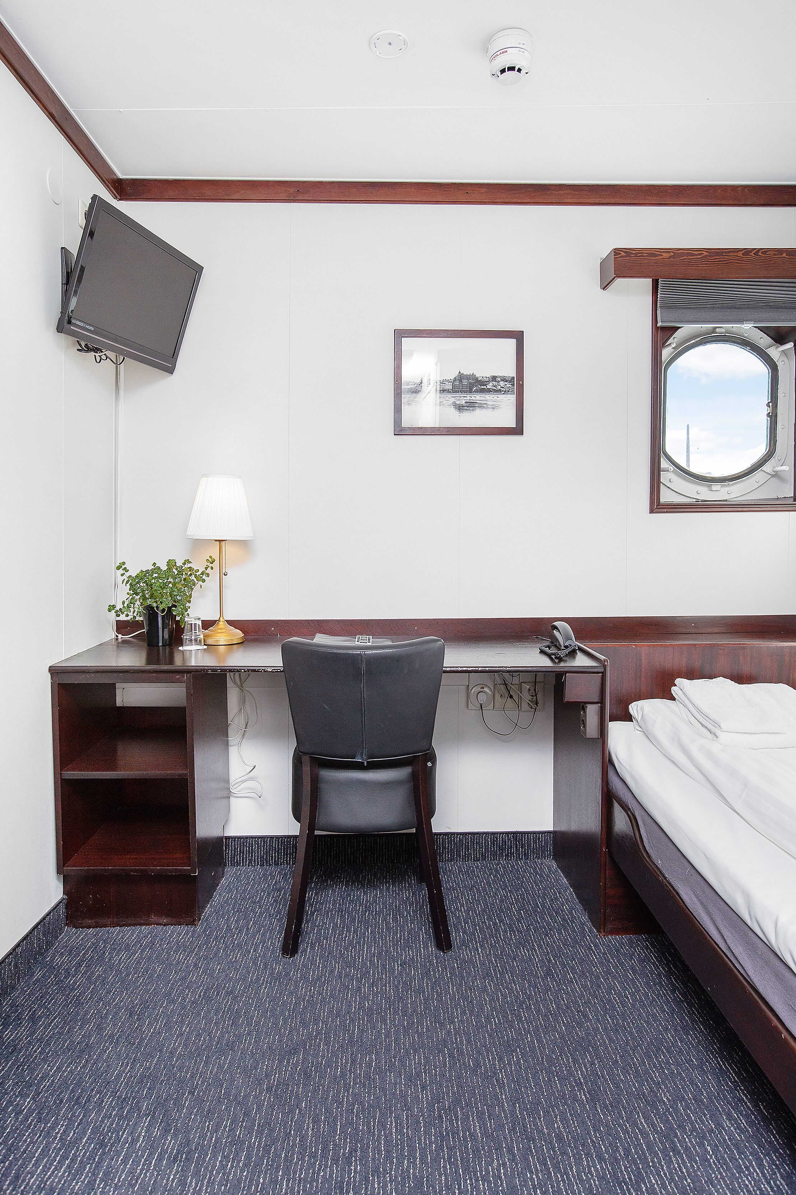 Habitación de hotel con escritorio, silla, cama, televisión, lámpara y un cuadro en la pared.